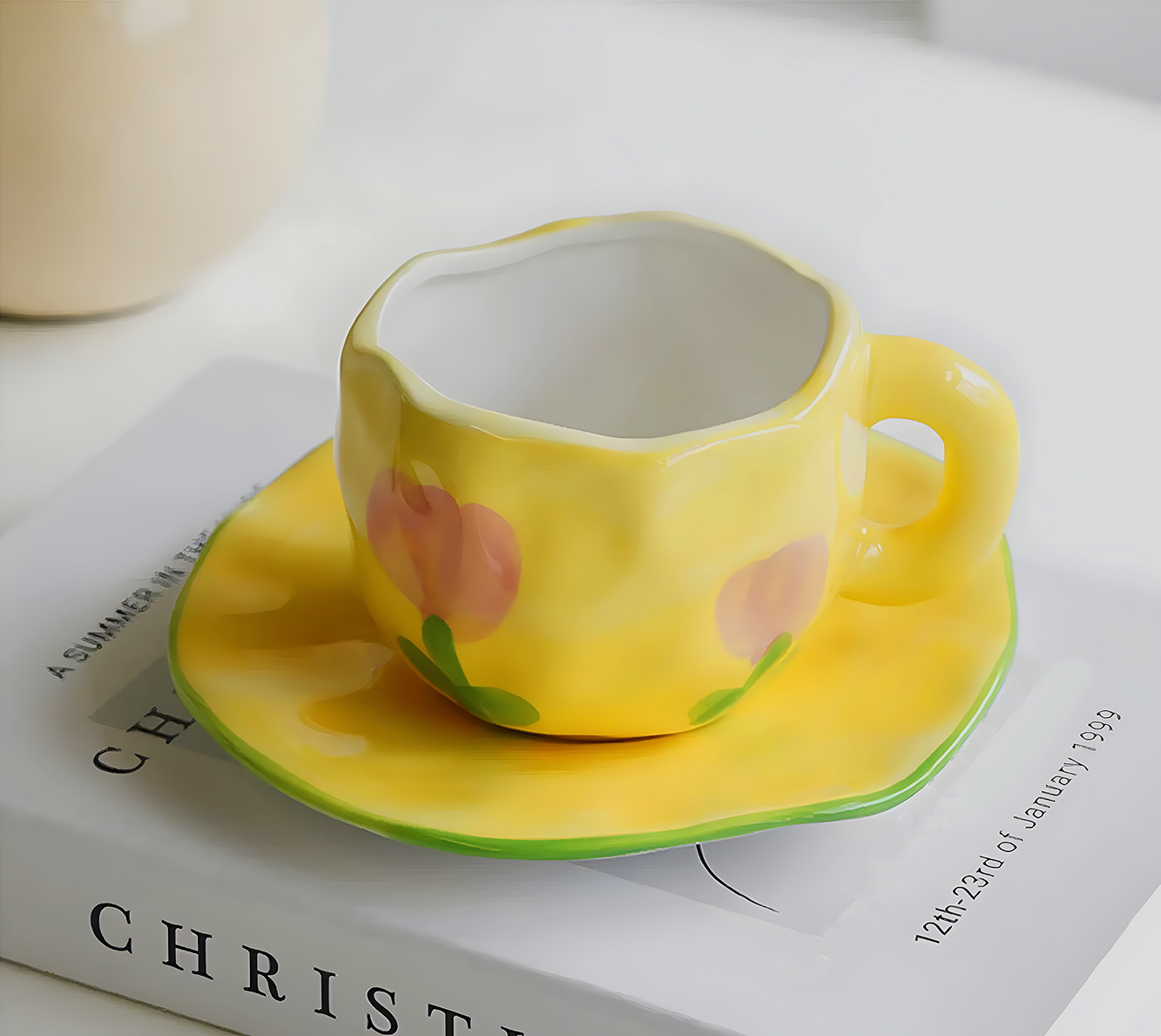 a ceramic yellow base with pink tulip mug and saucer on top of a book