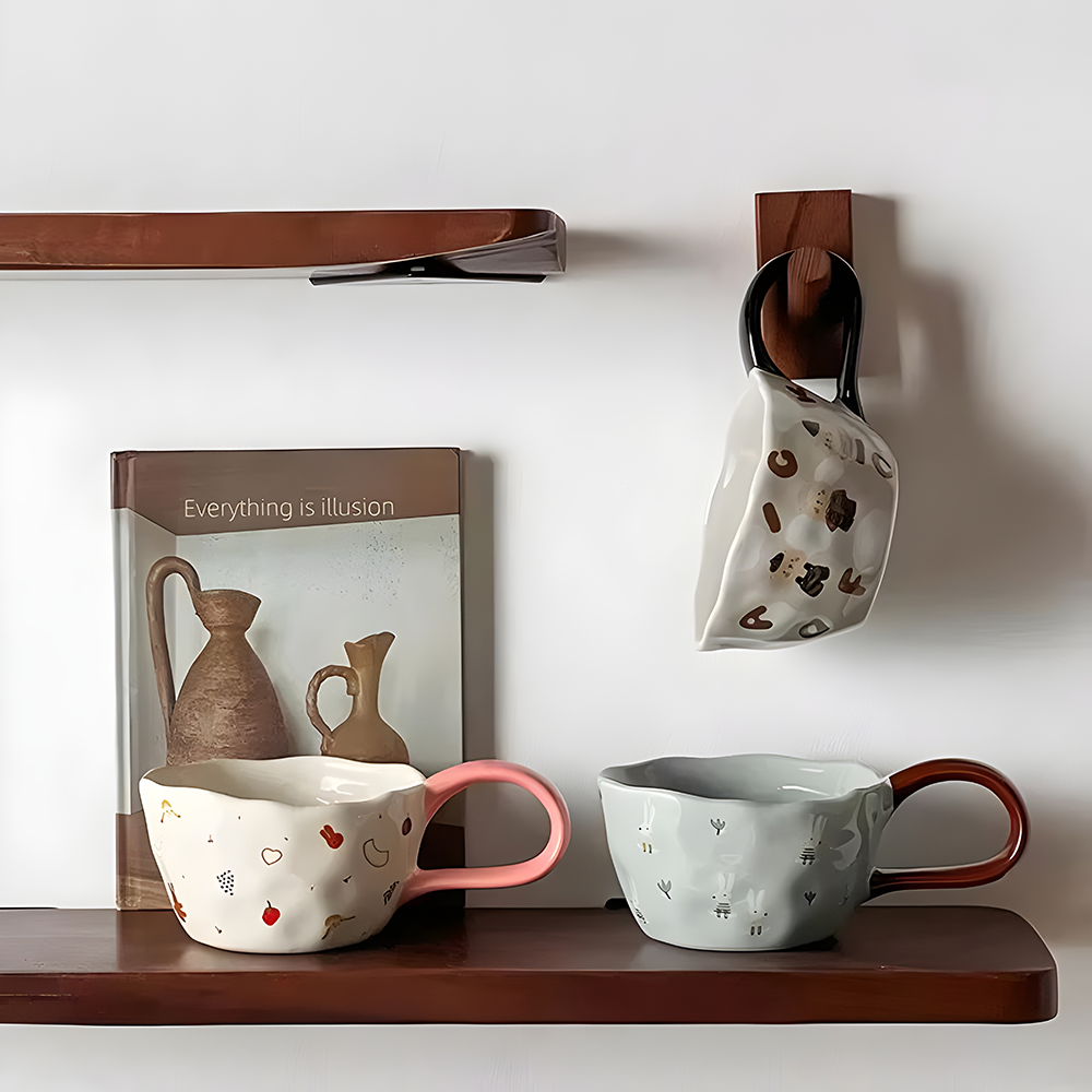 a pink big loop handle mug, a brown and blue big loop handle mug and a book on a wood shelf, a black and grey big loop handle mug hanging on the wall