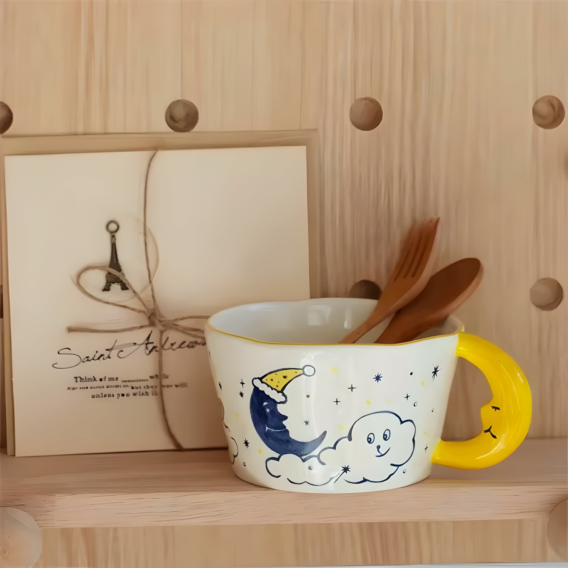 a moon shaped handle cearmic mug with blue moon, cloud, a dog and stars, on a wooden shelve, a wood fork and a soon inside the mug