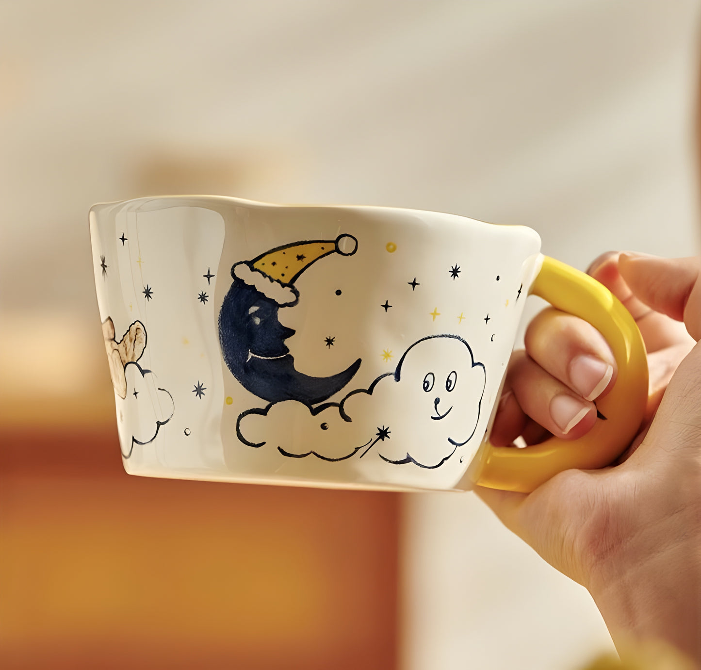 a hand holding a moon shaped handle cearmic mug with blue moon, cloud, a dog and stars